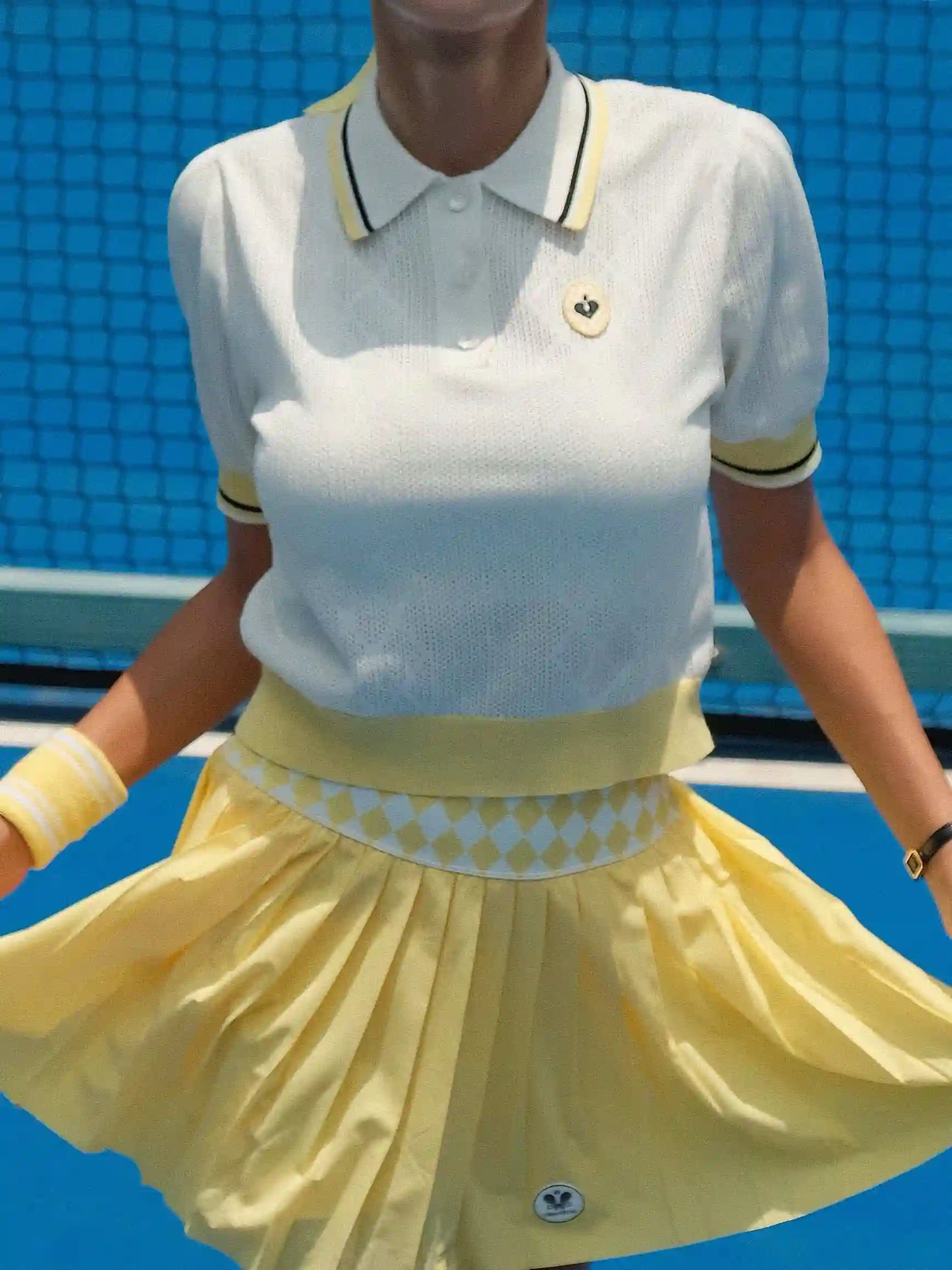 Person wearing a white polo shirt with yellow accents and a yellow skirt on a blue background