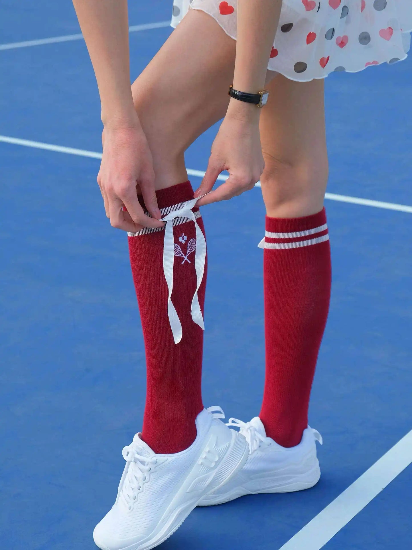 Person wearing red knee-high socks with white ribbons on a blue court.