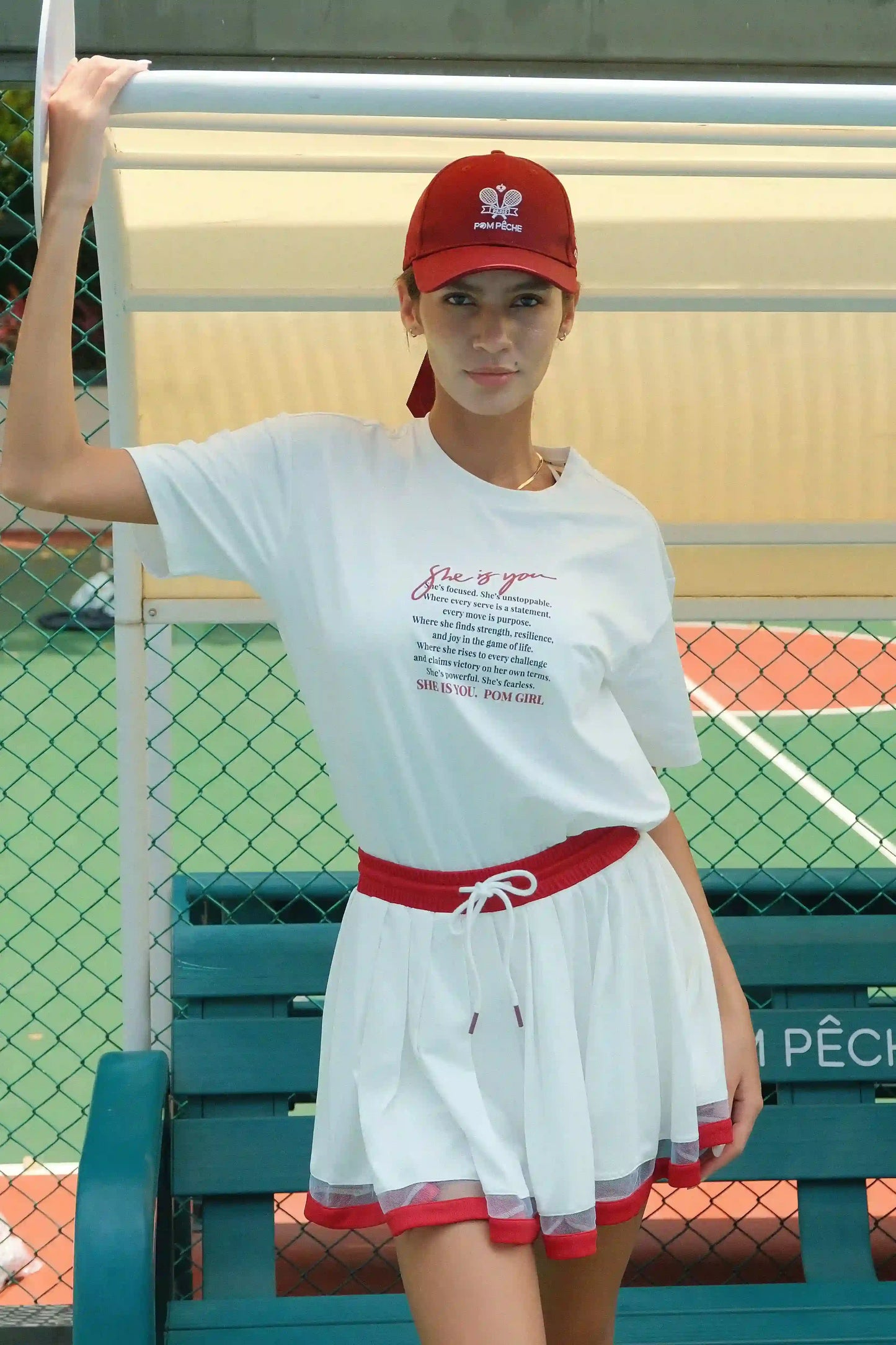 Person wearing a white t-shirt and red skirt with a red cap on a tennis court.