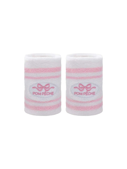White tennis wristbands with soft pink stripes, featuring embroidered bow and logo details.
