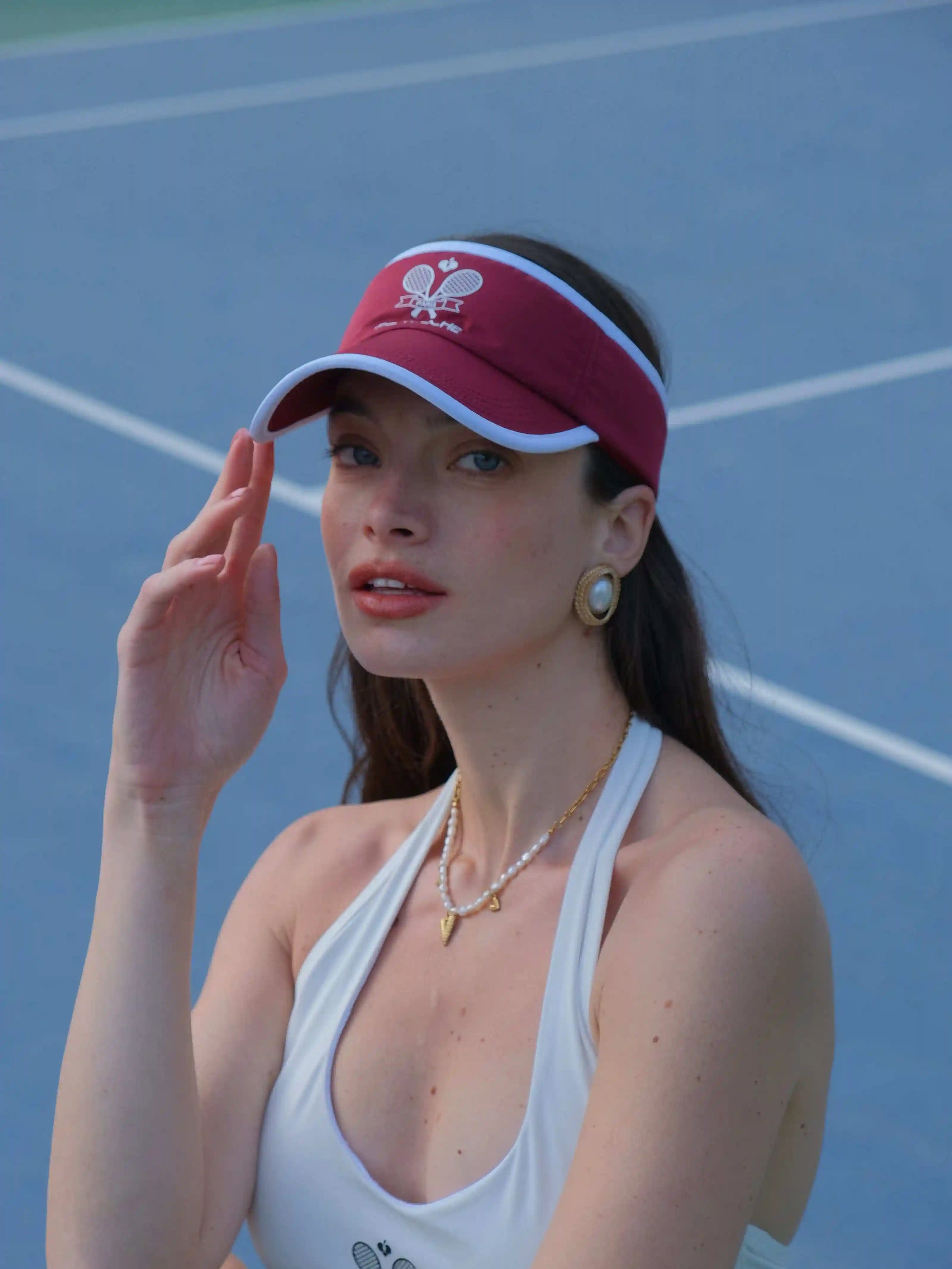 Woman wearing a red visor and white tank top on a tennis court