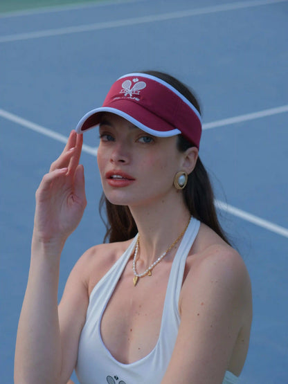 Woman wearing a red visor and white tank top on a tennis court